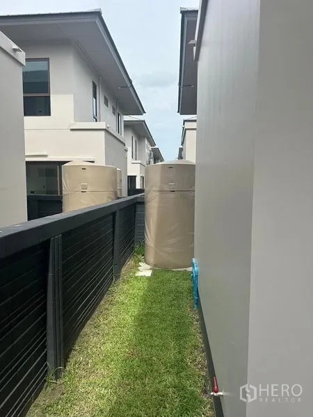 Detached House for rent in Bang Kapi, Bangkok - Narrow side yard with grass strip and water storage tanks beside the fence.