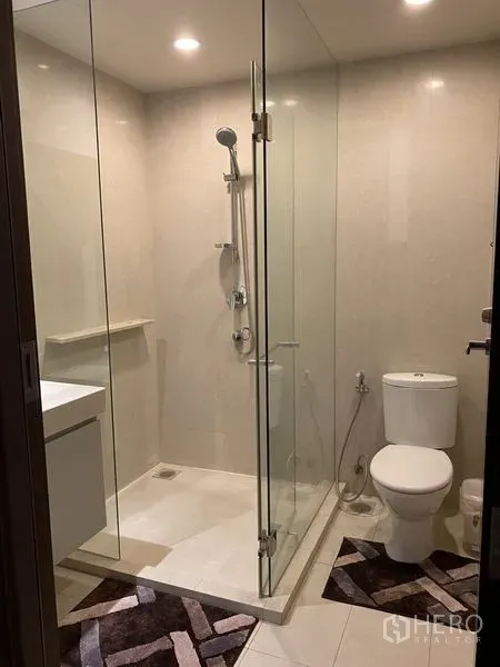 公寓 出租在Watthana, Bangkok - 浴室配玻璃淋浴房、坐便器与筒灯，米色墙地砖。