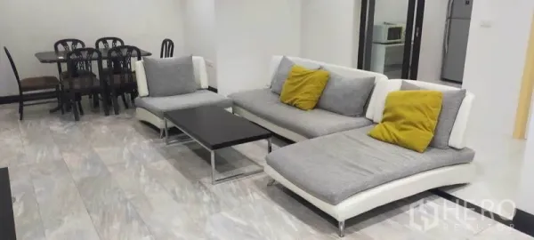 คอนโด ให้เช่าในWatthana, Bangkok - โซฟาแบบเชสสองตัวพร้อมหมอนสีเหลือง ถัดไปเป็นครัวและโต๊ะอาหาร