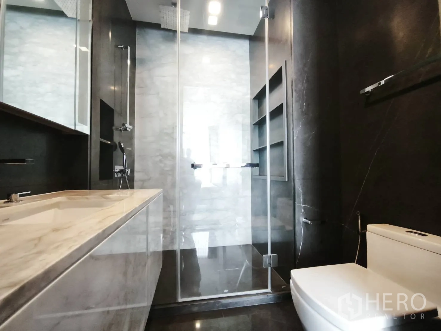Condominium for rent in Watthana, Bangkok - Modern bathroom with marble vanity, glass shower enclosure, and toilet.