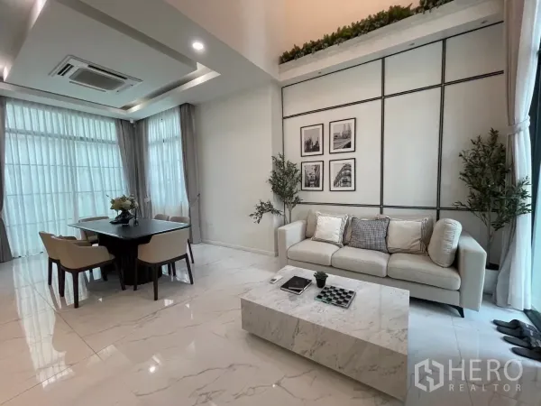 Detached House for rent in Lat Phrao, Bangkok - Bright living and dining area with marble-look floors, sofa set and dining table beside floor-to-ceiling windows.