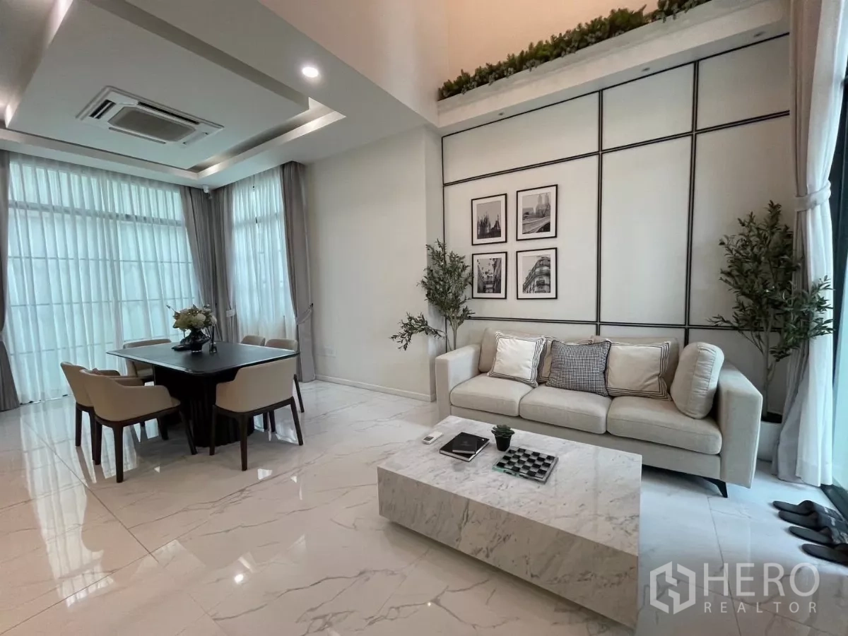 Detached House for rent in Lat Phrao, Bangkok - Bright living and dining area with marble-look floors, sofa set and dining table beside floor-to-ceiling windows.
