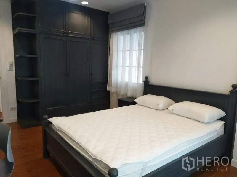 联排别墅 出租在Mueang Samut Prakan, Samut Prakan - 卧室配深色木床、嵌入式衣柜与纱帘窗户。