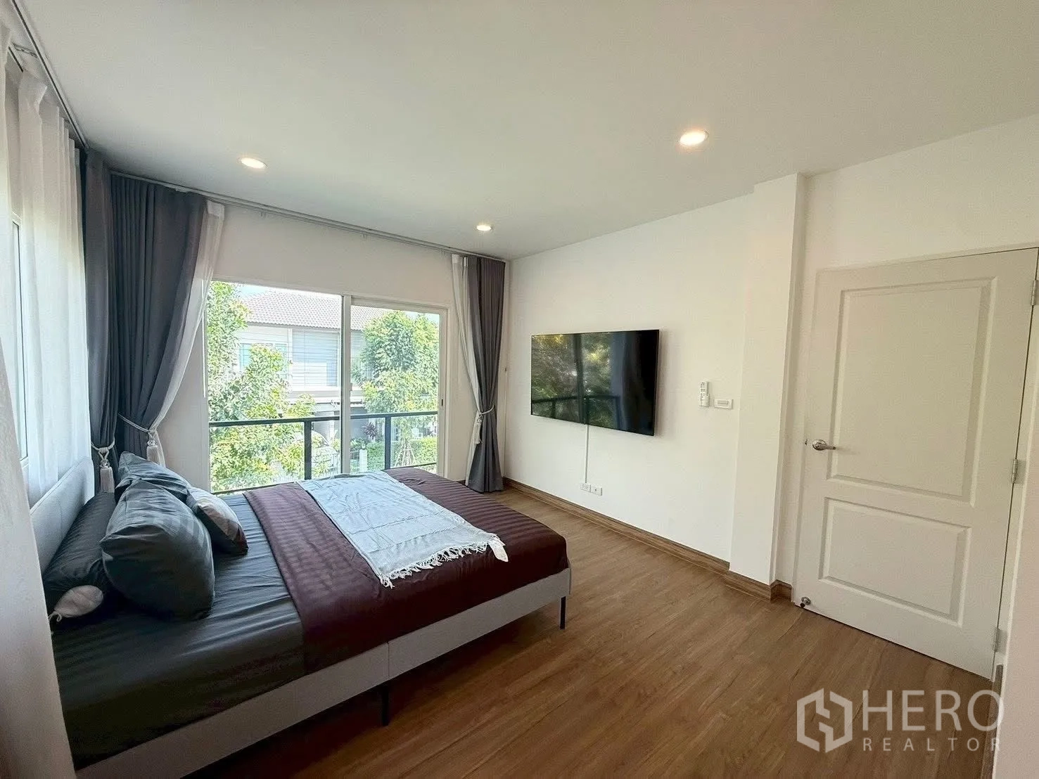 Detached House for rent in Prawet, Bangkok - Bedroom with large windows, wall-mounted TV and wood flooring.