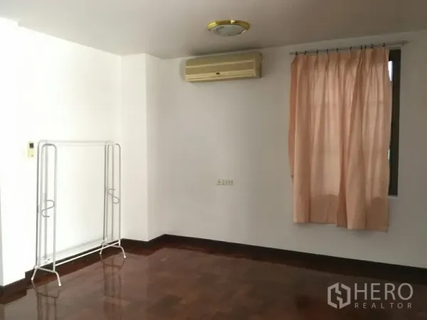 บ้าน ให้เช่าหรือขายในHuai Khwang, Bangkok - ห้องเรียบง่ายมีผ้าม่าน แอร์แขวนผนัง และราวแขวนเสื้อผ้าบนพื้นไม้