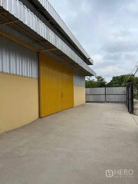 货栈 出租在Lat Krabang, Bangkok - 仓库外观展示宽大的黄色金属装卸门、混凝土硬地与围栏大门。