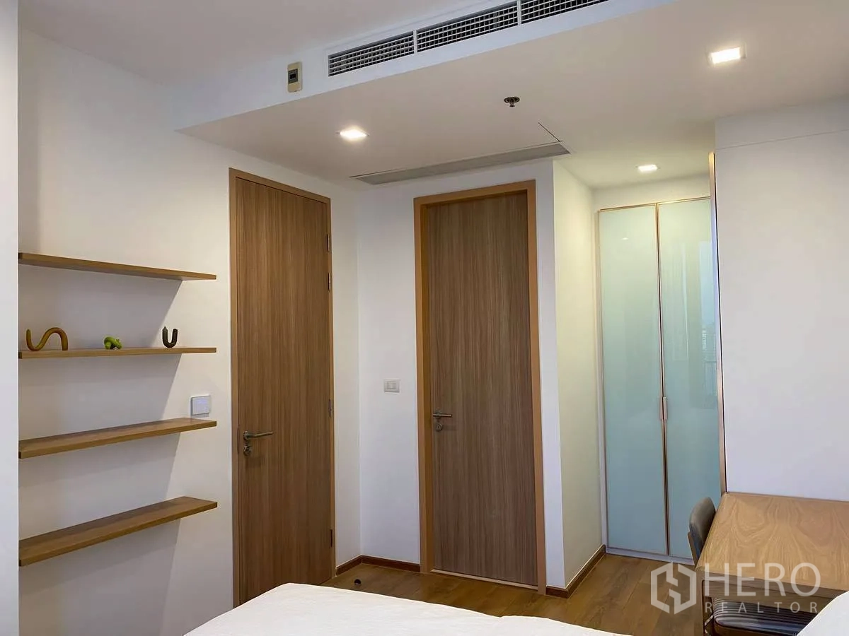 Condominium for rent in Watthana, Bangkok - Minimal bedroom with wood doors, open shelving, desk, and frosted-glass wardrobe.