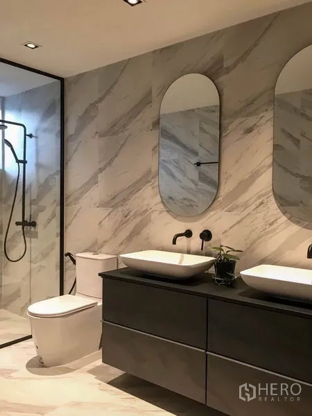 Townhouse for rent in Khlong Toei, Bangkok - Elegant bathroom with marble-pattern tiles, double vanity with oval mirrors and a glass shower.