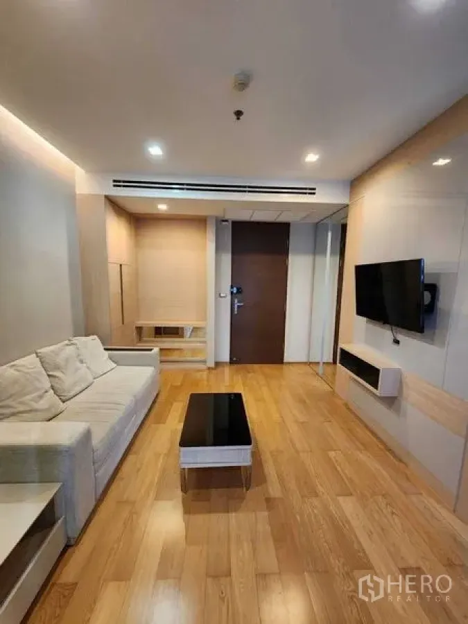 Condominium for sale in Ratchathewi, Bangkok - Another view of the living room showing sofa, mounted TV and minimalist built-in storage.