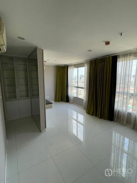 Condominium for sale in Suan Luang, Bangkok - Open-plan room with wraparound windows, built-in shelving and glossy white floor tiles.