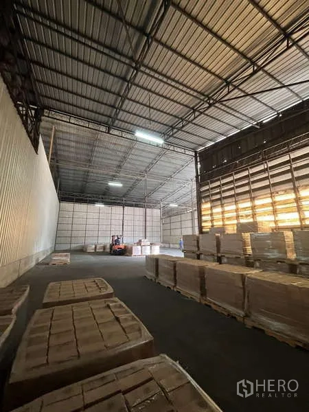 Warehouse for rent in Rat Burana, Bangkok - Deep-bay warehouse showing steel frame ceiling, pallets and a roller shutter entry.