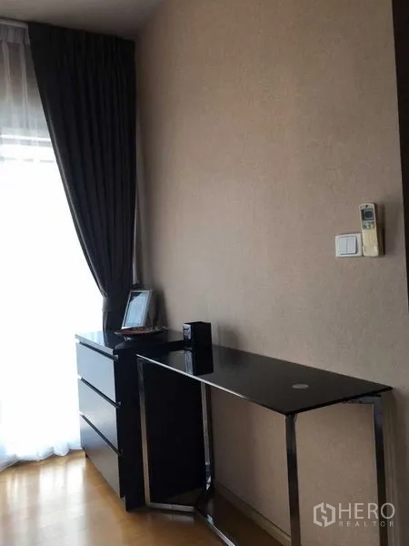 Condominium for sale in Khlong San, Bangkok - Slim black-glass desk and drawer unit beside full-length curtains.