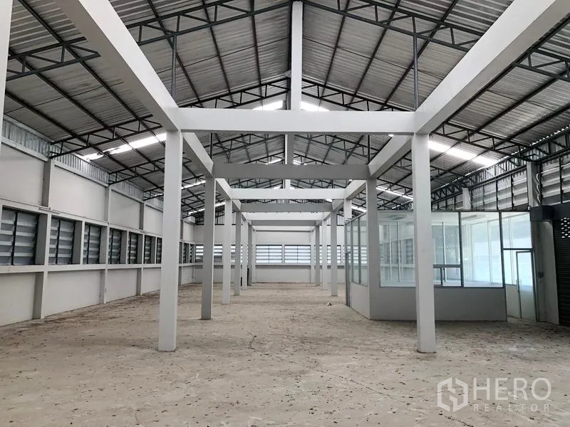 工厂 出租在Bang Bua Thong, Nonthaburi - 厂房内部空间宽敞，钢结构高屋顶、白色立柱与百叶通风窗。
