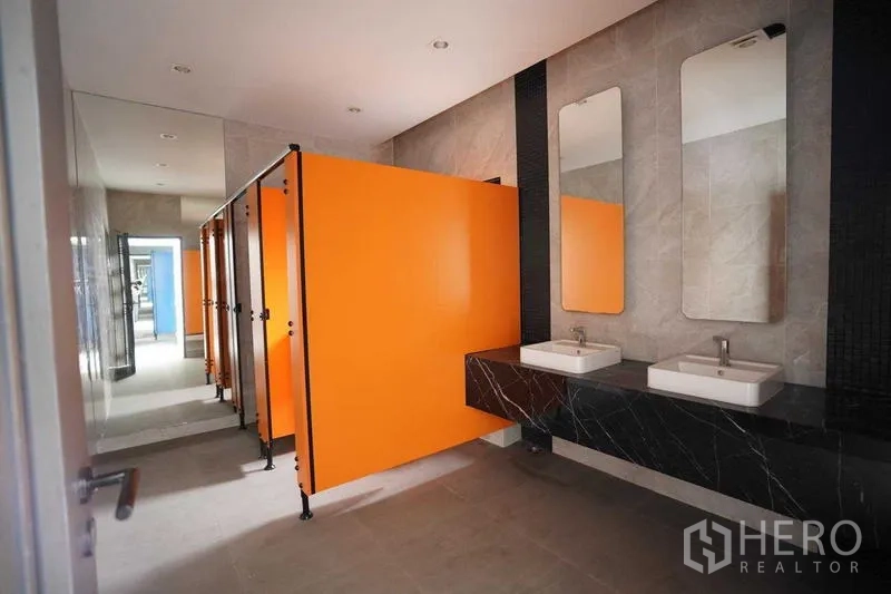 独立商业地产 出租在Bang Na, Bangkok - 洗手间走道设橙色隔间，黑色台面上双台盆。