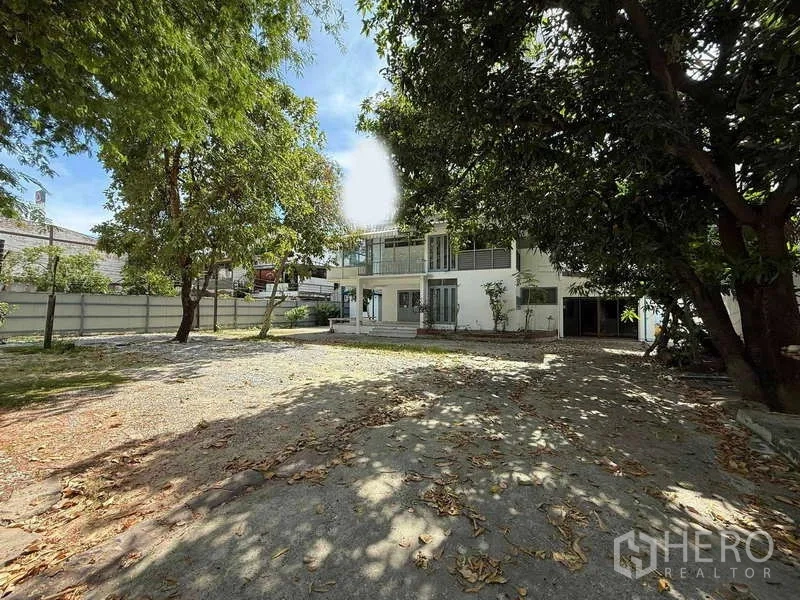 独立式住宅 出租在Watthana, Bangkok - 宽敞的树荫前院，通往两层白色独栋住宅。