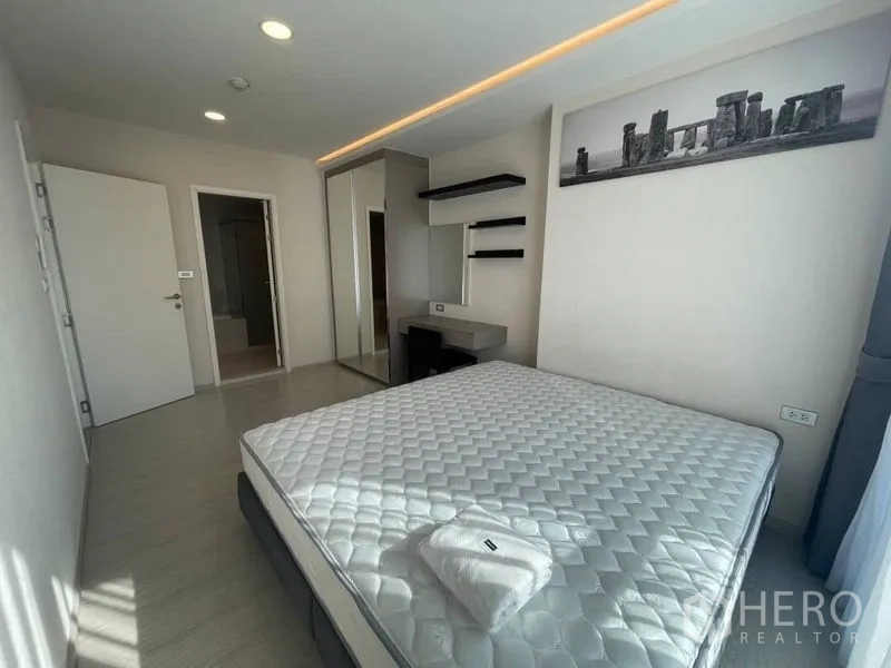 Condominium for rent in Khlong Toei, Bangkok - Bedroom with wardrobe, desk, and doorway to bathroom, filled with natural light.