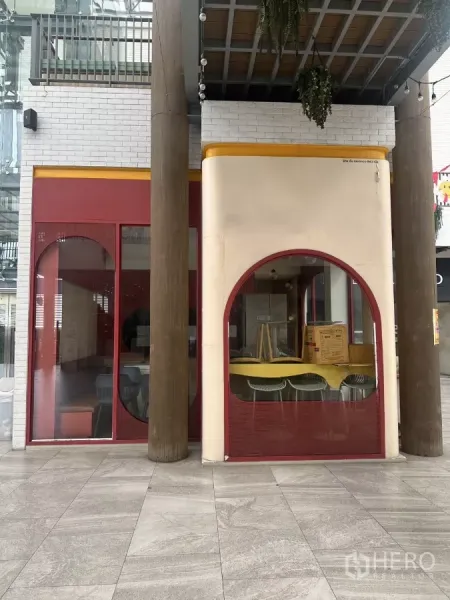 零售空间 出租在Khlong Toei, Bangkok - 底层店面，红色拱形玻璃立面与木柱，位于有顶中庭。