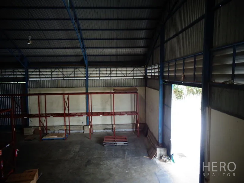 Warehouse for rent or sale in Lat Lum Kaeo, Pathum Thani - Corner bay with open roller door, wall ventilation louvers and empty shelving.