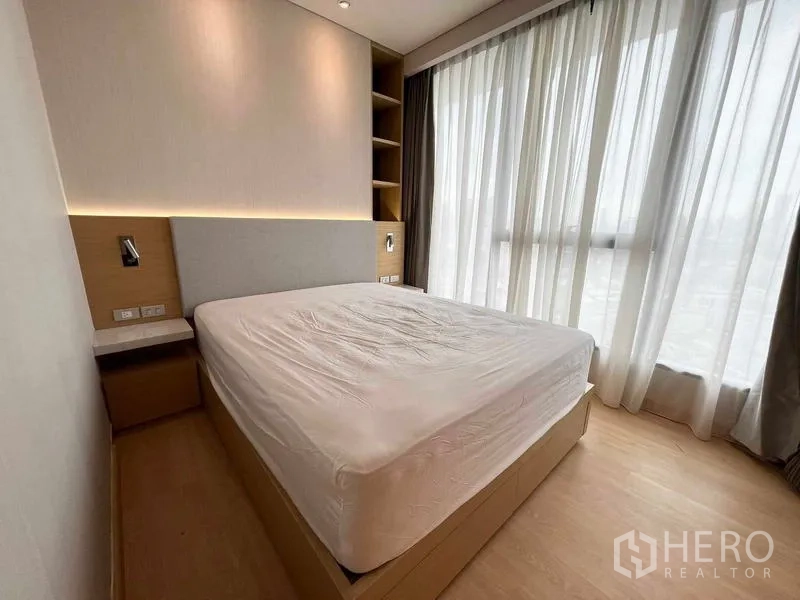 คอนโด ให้เช่าหรือขาย - ห้องนอนพร้อมหน้าต่างเต็มบาน ผ้าม่านโปร่ง และหัวเตียงไฟ LED แสงเมืองรำไร