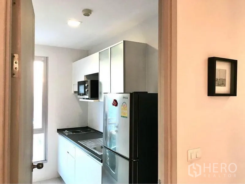 Condominium for rent in Huai Khwang, Bangkok - Compact kitchen with window, white cabinetry and stainless fridge.