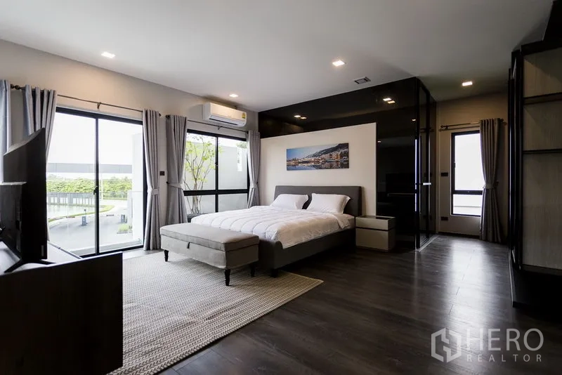 联排别墅 出租在Samut Prakan - 宽敞主卧，落地窗、木地板与电视。