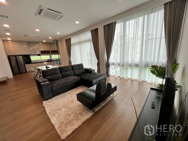 Detached House for rent or sale in Saphan Sung, Bangkok - Bright living room with floor‑to‑ceiling windows, L‑shaped sofa, rug and open kitchen.