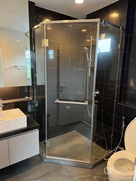 Detached House for rent in Bang Kapi, Bangkok - Contemporary bathroom featuring a corner glass shower, dark wall tiles, vanity and toilet.