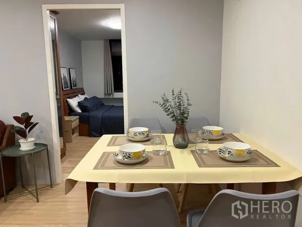 Condominium for rent in Ratchathewi, Bangkok - Dining area set for four with centerpiece, wood floors, and a doorway opening to a cozy bedroom.