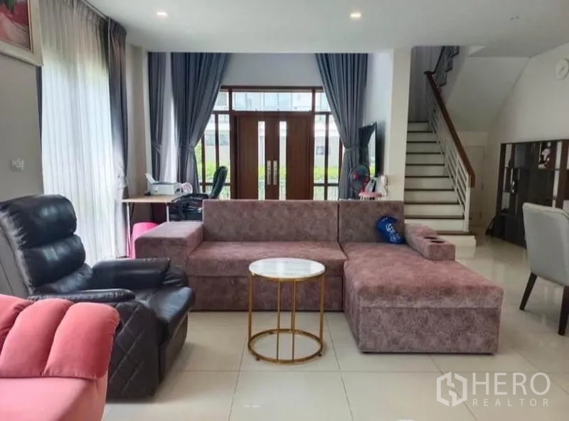 独立式住宅 出租 - 宽敞客厅，L 形沙发、休闲躺椅与通往二楼的楼梯。