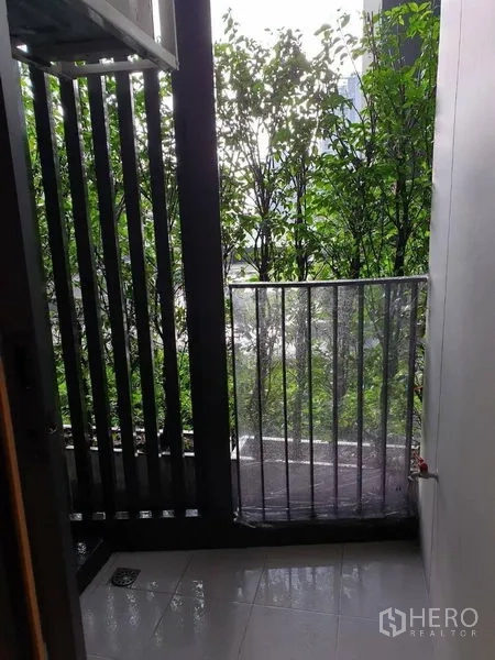 Condominium for sale in Watthana, Bangkok - Compact condo balcony with privacy slats, tiled floor and leafy green outlook.