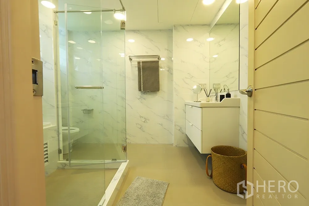 Condominium for rent in Watthana, Bangkok - Modern bathroom with glass shower, white marble-effect walls and a floating vanity.