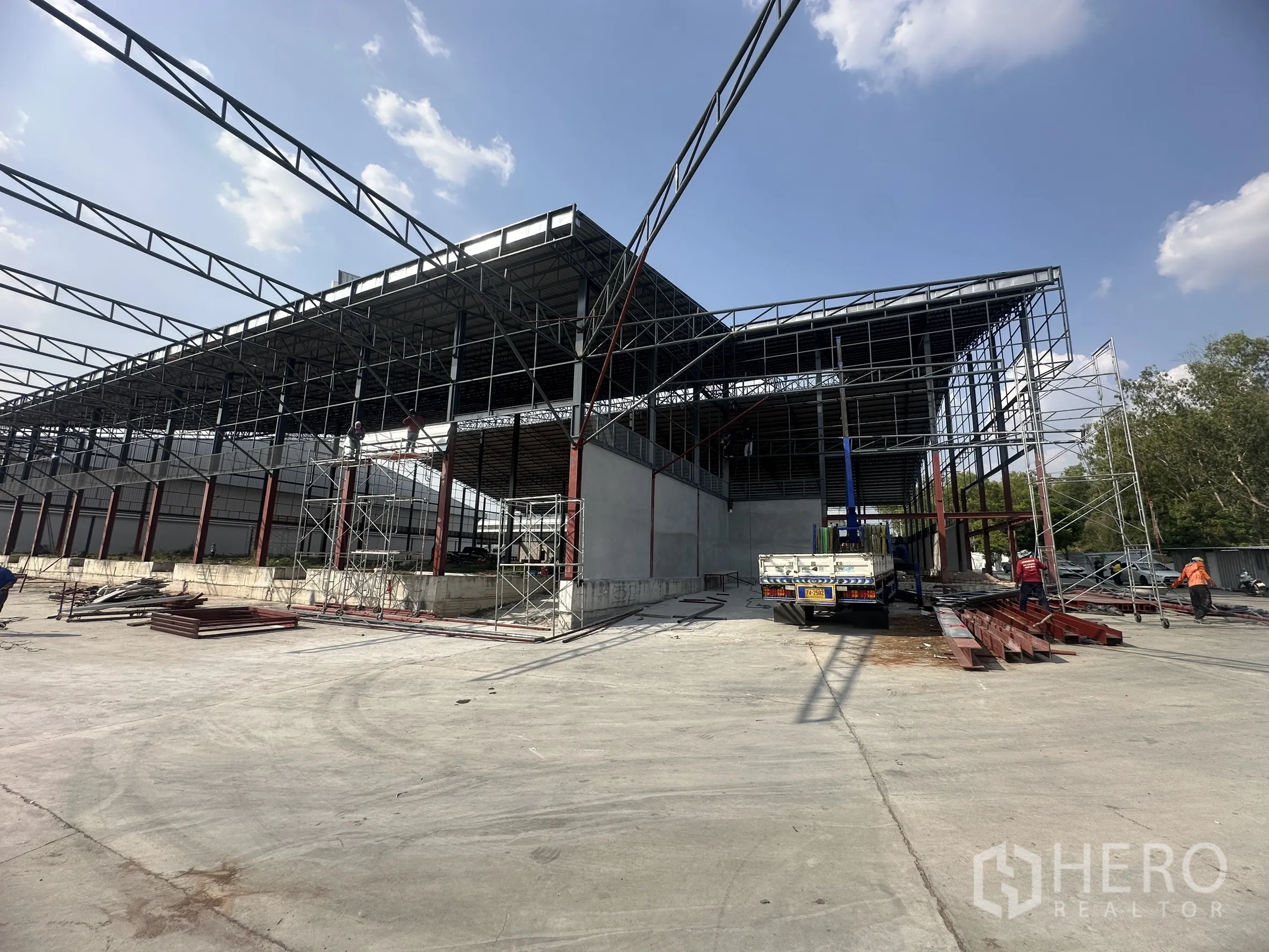 Factory for rent in Si Racha, Chon Buri - Warehouse structure with scaffolding and trucks on a large concrete apron.