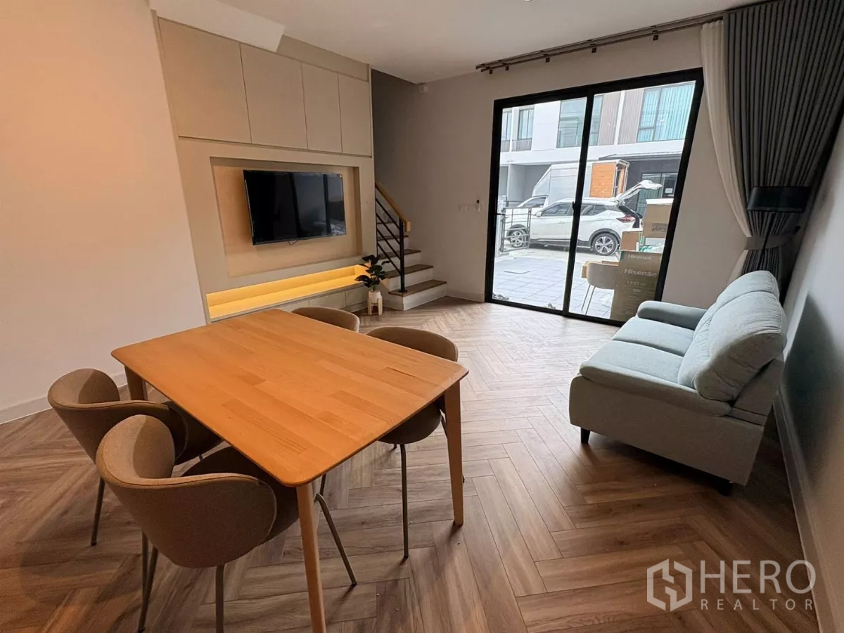 Townhouse for rent in Bang Phli, Samut Prakan - Dining area facing a TV feature wall with sliding doors to the patio and stairs to the second floor.