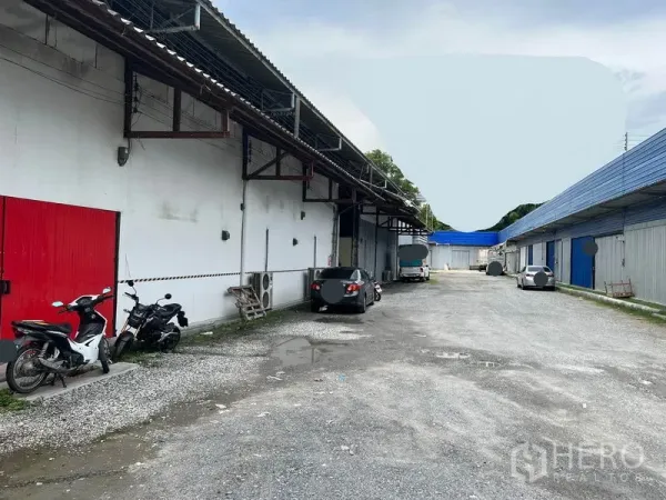 คลังสินค้า ให้เช่าในMueang Samut Prakan, Samut Prakan - ลานโกดังทางเข้าโรยหินกว้าง ประตูสีแดง พร้อมที่จอดรถและรถจักรยานยนต์