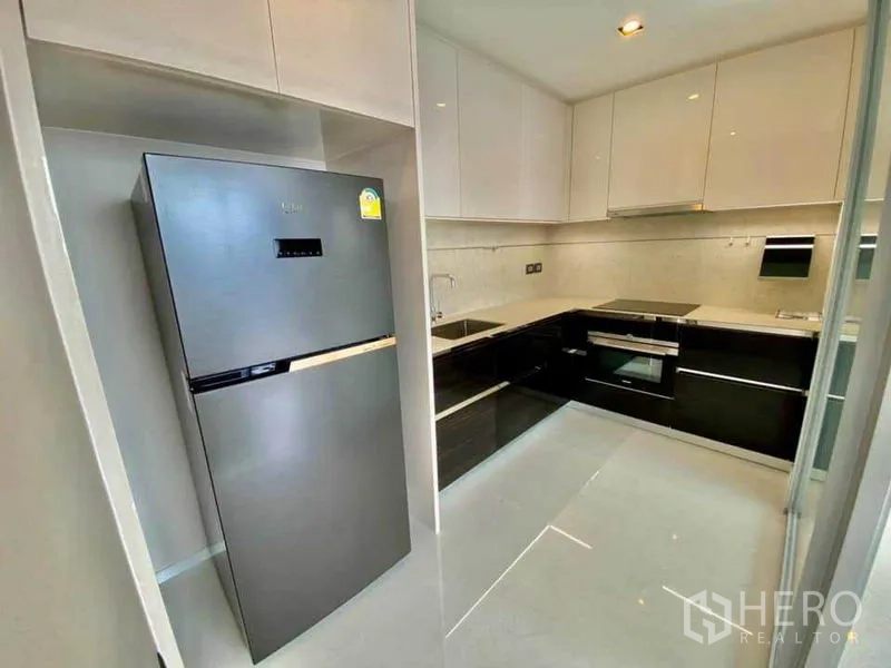Condominium for rent in Sathon, Bangkok - Modern U-shaped kitchen with glossy cabinets and stainless refrigerator.