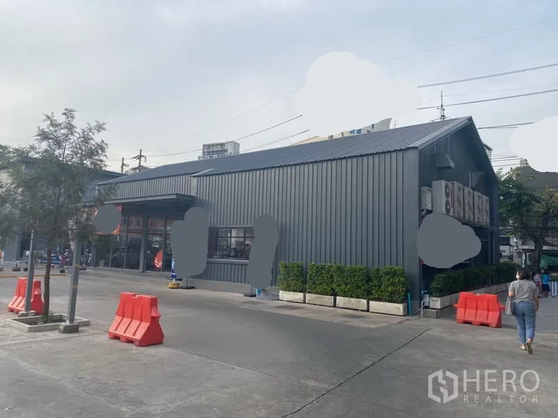 零售空间 出租在Khlong Toei, Bangkok - 建筑转角视角，金属外墙配景观花槽与雨棚。