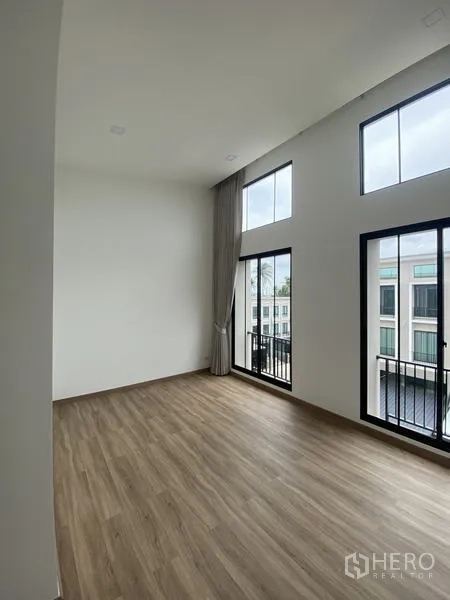 Townhouse for rent or sale in Bang Khae, Bangkok - Spacious upper room with high ceiling, wood flooring, and multiple tall windows with Juliet balconies