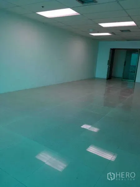 Office Space for rent in Huai Khwang, Bangkok - Empty office room with glossy tile flooring, drop ceiling lights, and a glass entry door.