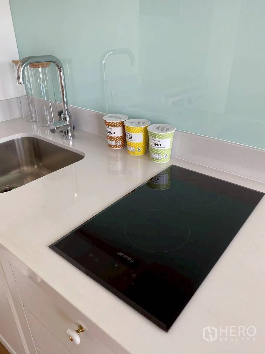 Condominium for rent in Watthana, Bangkok - Modern kitchenette close-up showing sink and induction cooktop.