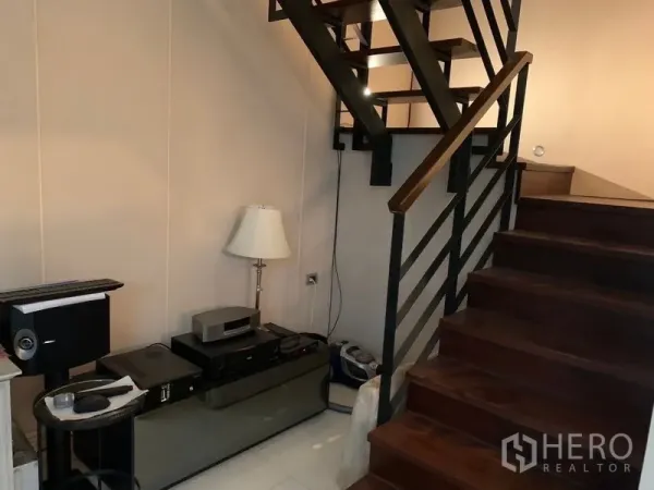 Townhouse for sale in Watthana, Bangkok - Wood staircase with metal railing and an under-stair storage niche in the corridor.