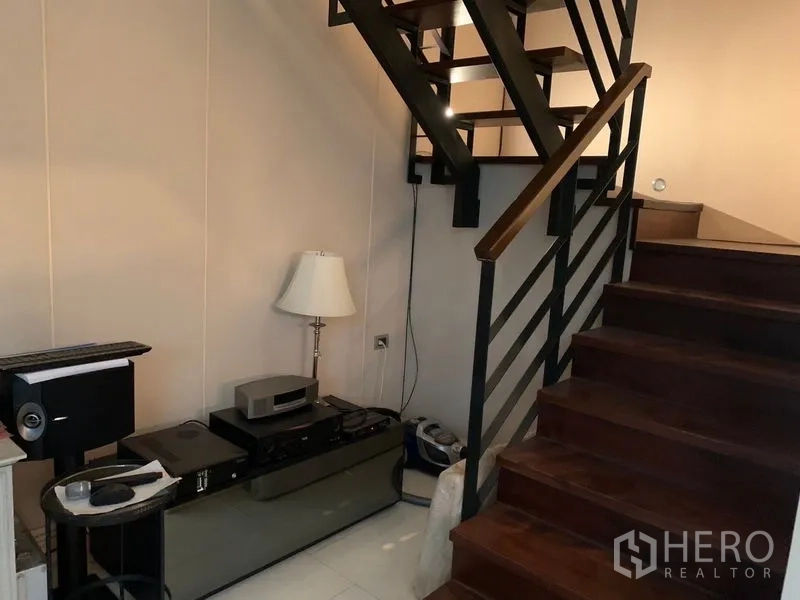 Townhouse for sale in Watthana, Bangkok - Wood staircase with metal railing and an under-stair storage niche in the corridor.