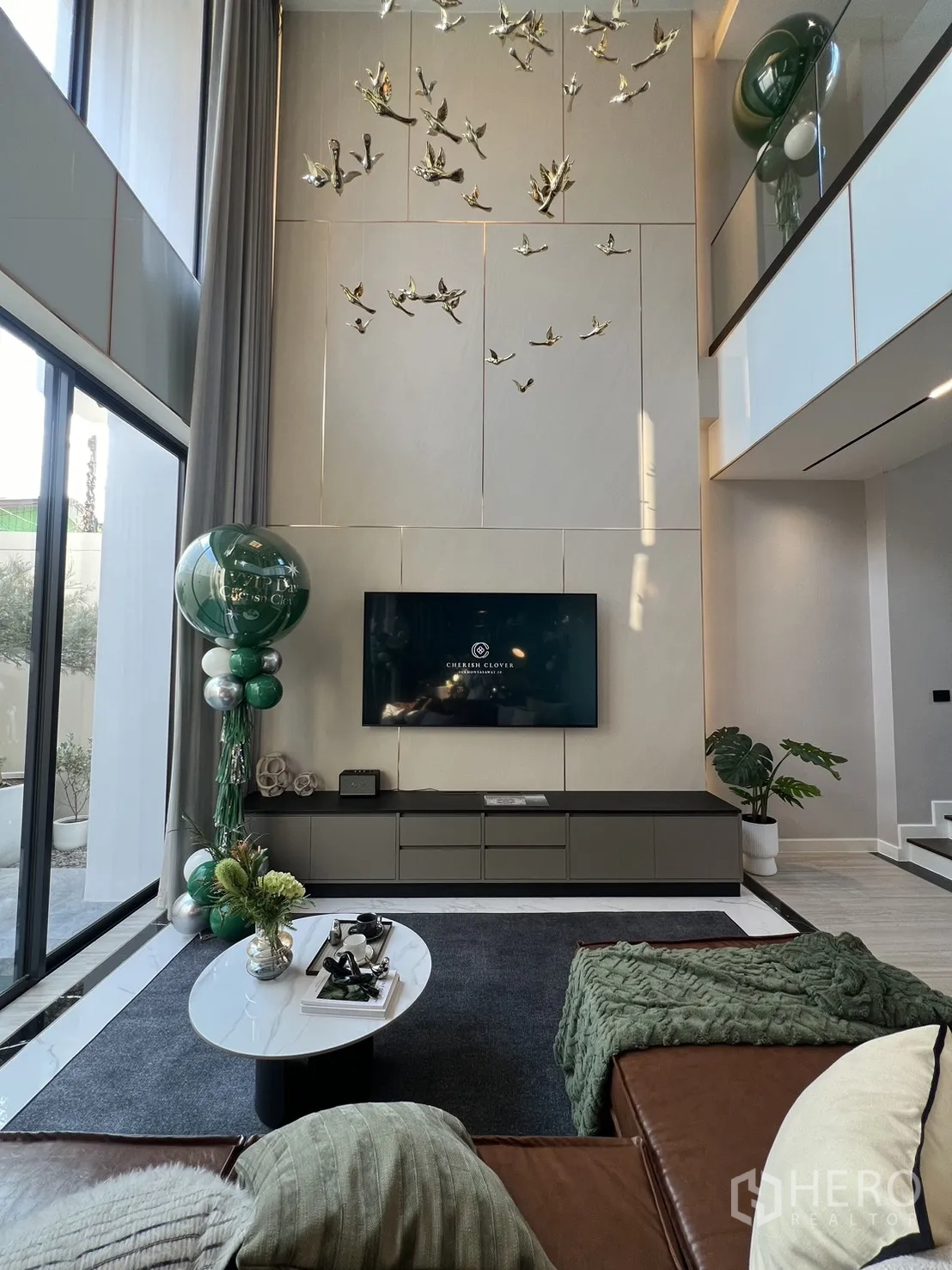 บ้าน ขายในLat Phrao, Bangkok - ห้องนั่งเล่นเพดานสูงติดผนังทีวีและงานประดับนก พร้อมหน้าต่างบานใหญ่