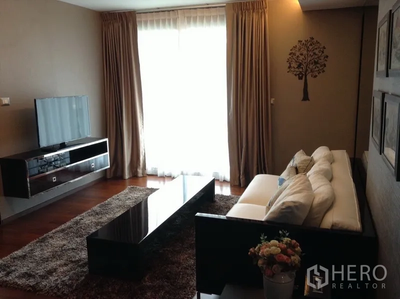 Condominium for rent in Watthana, Bangkok - Cozy living room with long coffee table, TV console, large window with curtains and a shaggy rug.