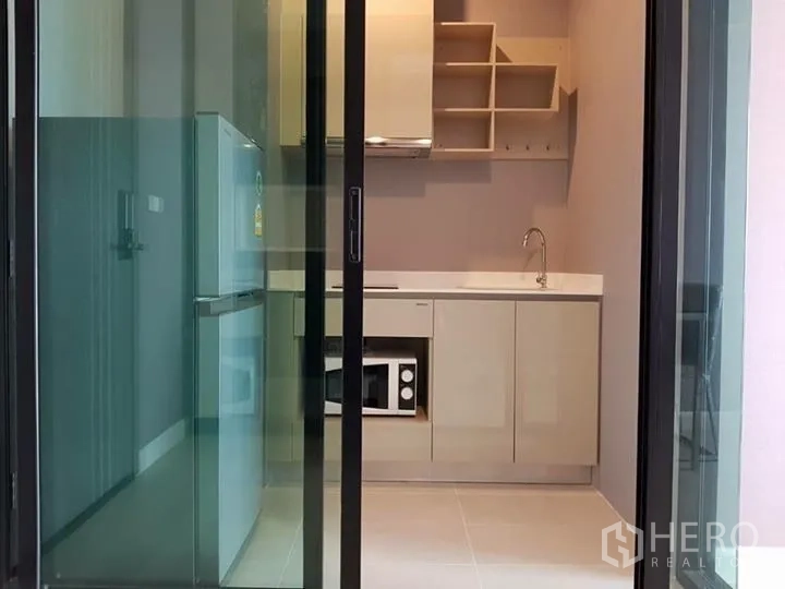 Condominium for rent in Pathum Wan, Bangkok - Compact enclosed kitchen behind sliding glass with cabinets, fridge and microwave.