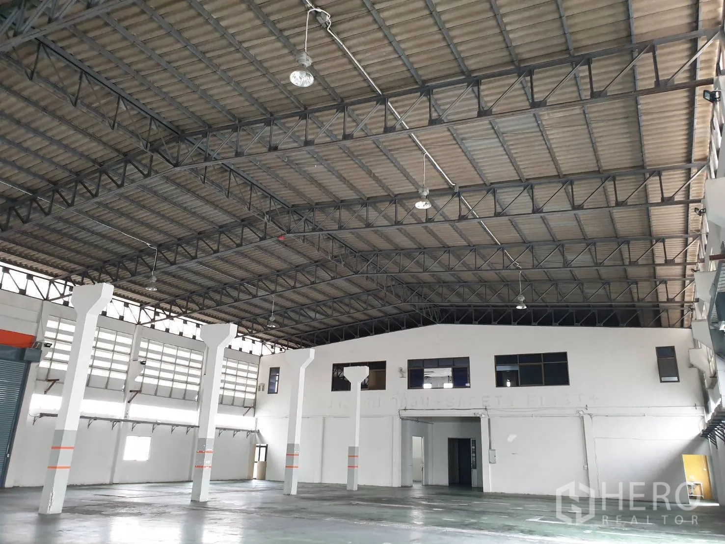 工厂 出租在Bang Pakong, Chachoengsao - 仓库内部空间开阔，钢结构屋架挑高，吊灯与白色支柱清晰可见。