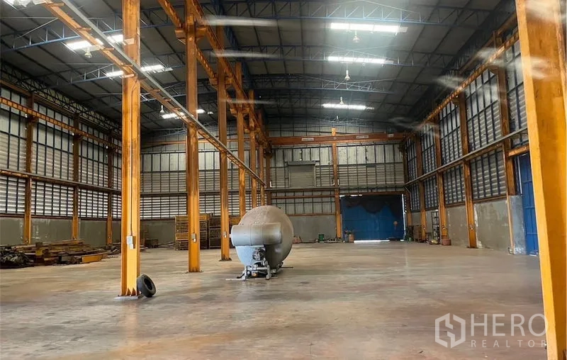 Factory for rent in Samut Songkhram - Wide warehouse hall with skylights, ventilation louvers, crane beam rails and large blue sliding doors in Amphawa.