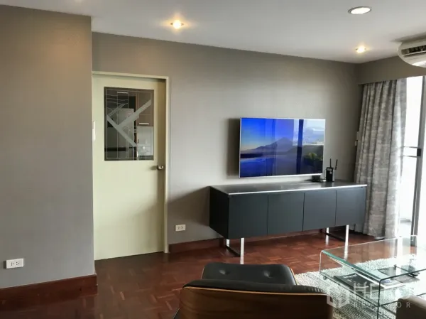 Condominium for rent in Watthana, Bangkok - Modern living room with wall-mounted TV, parquet floors, glass coffee table and balcony access.