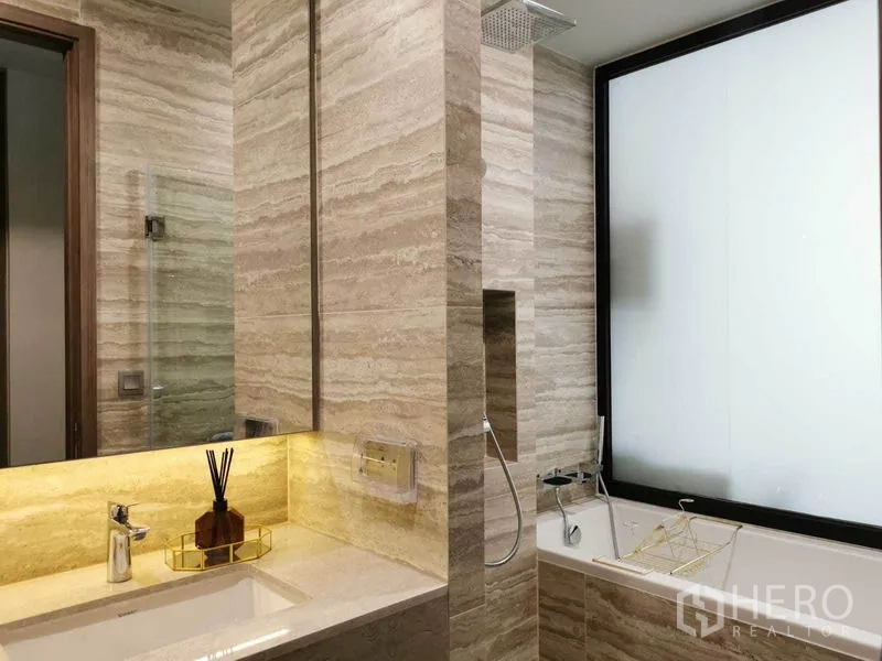 Condominium for rent in Watthana, Bangkok - Luxury bathroom featuring stone tiles, a bathtub, rain shower, and backlit vanity.