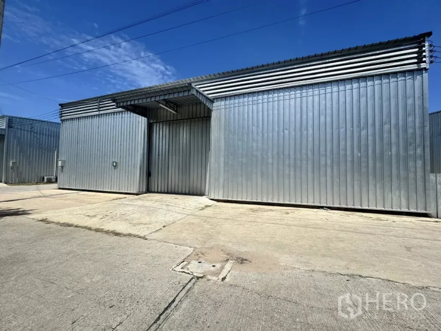 Warehouse for rent in Bang Lamung, Chon Buri - Corrugated steel warehouse exterior with large sliding door and wide concrete yard in Bang Lamung.