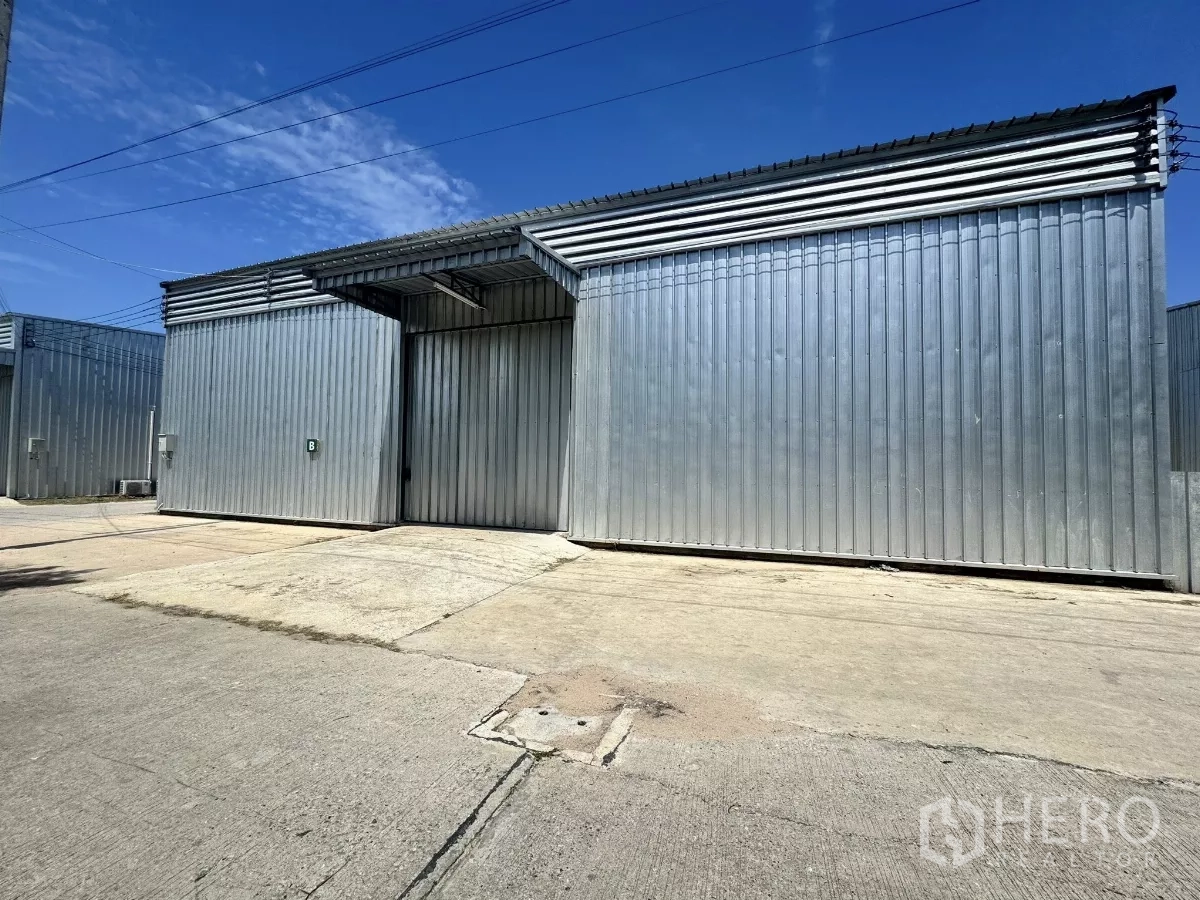 Warehouse for rent in Bang Lamung, Chon Buri - Corrugated steel warehouse exterior with large sliding door and wide concrete yard in Bang Lamung.